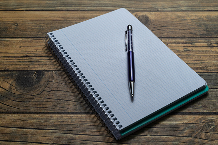 Empty notebook sheet with a pen on wooden background and copy sp