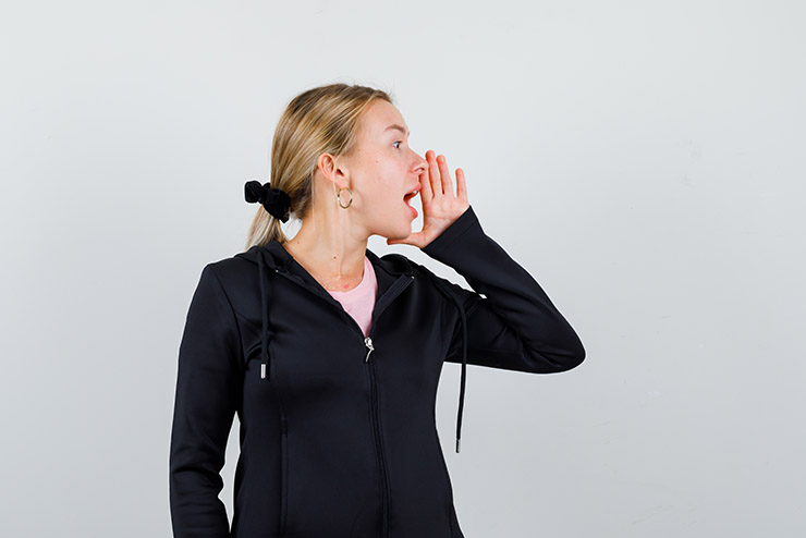 young blonde woman holding hand near mouth while telling secret