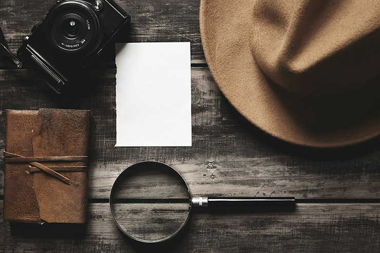 Photo camera, notebook, hat, magnifier, paper on black table