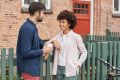 Young diverse couple meet in rural street, stand near green fence and brick house, have positive talk, drink coffee, discuss plans on weekend, plan to ride bicycle together. Interracial friendship