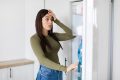 Shocked woman looking into fridge, displaying surprise and disbelief about lack of food, home kitchen interior setting